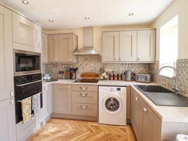 A kitchen with beige cabinets patterned tile backsplash and wooden floor at Varley Villa in Newtown