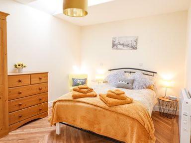 A bedroom with a bed covered in orange bedding and folded towels a wooden dresser a yellow chair with a cushion and bedside tables at Varley Villa in Newtown