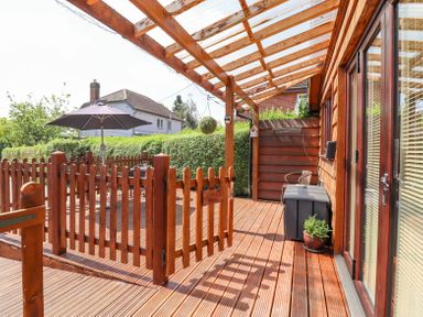 A wooden deck with a picket fence and gate under a transparent roof with a patio table and umbrella at Varley Villa in Newtown