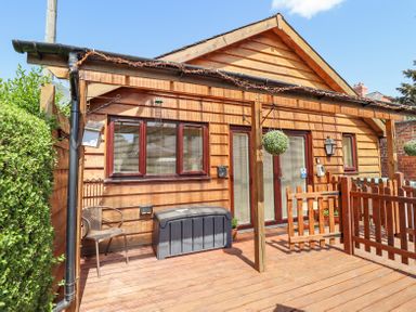 A wooden deck with a chair a storage box hanging plants and a wooden fence at Varley Villa in Newtown
