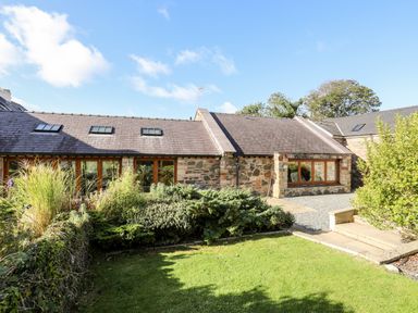 A stone house with skylights and windows surrounded by green shrubs and a lawn at Clynnog House in Dwyran near Newborough