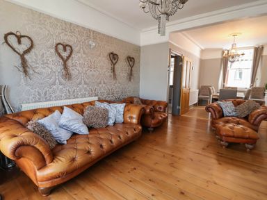 A living room with brown leather sofas and chairs wooden floor and wall decorations at Albany in Looe