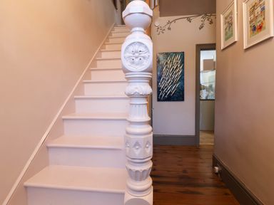 A white staircase with a decorative banister in a hallway with wooden floor and artwork on walls at Albany in Looe