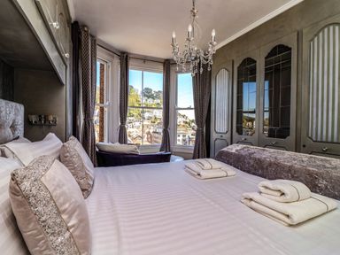 A bedroom with a bed and pillows near windows with curtains and a chandelier above at Albany in Looe