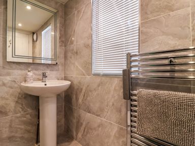 A bathroom with a pedestal sink a mirror a window with blinds and a heated towel rail at Albany in Looe