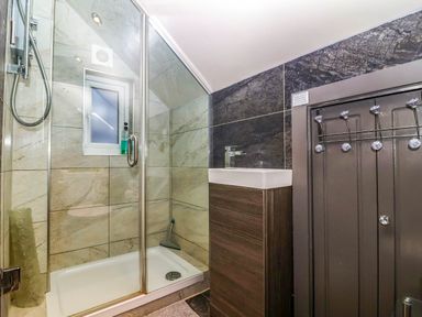 A bathroom with a glass shower enclosure a small window a sink with a cabinet and hooks on a wooden panel at Albany in Looe