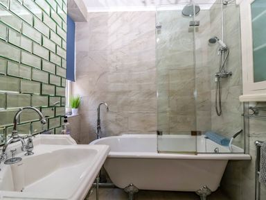 A bathroom with a white clawfoot bathtub with a shower head and glass screen a white sink with a chrome faucet and a wall with rectangular mirrors at Albany in Looe