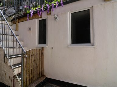 An outdoor stairway with a metal railing leading to a platform with a small wooden gate and two small windows above at Albany in Looe