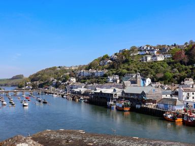 A river with boats docked alongside a town with houses on a hillside at Albany in Looe
