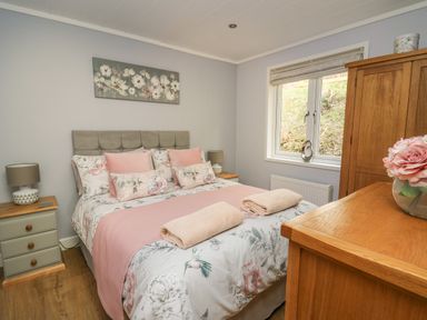A bedroom with a double bed pink bedding wooden furniture and a window at McAuliffe Lodge in Borth