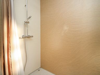 A shower area with a handheld showerhead and beige walls at McAuliffe Lodge in Borth