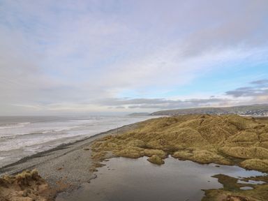 A beach with waves on the shore and grassy dunes with small water pools at McAuliffe Lodge in Borth