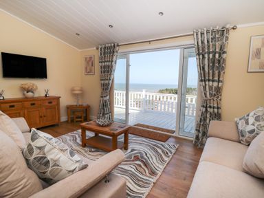 A living room with sofas coffee table wooden cabinet and glass doors opening to a balcony with a sea view at McAuliffe Lodge in Borth
