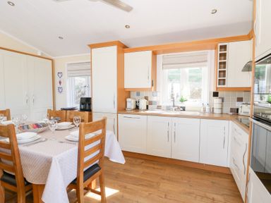 A kitchen with wooden chairs around a table set for dining and white cabinets at McAuliffe Lodge in Borth