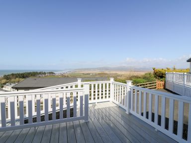 A deck with white railing overlooking rooftops and a distant coastline at McAuliffe Lodge in Borth