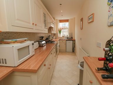 A galley kitchen with wooden countertops white cabinets a microwave toaster and wine bottles at Sandsend Sunset View in Whitby