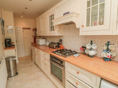 A kitchen with wooden countertops white cabinets a gas stove oven microwave and mug racks at Sandsend Sunset View Whitby