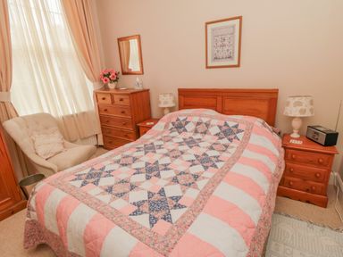 A bedroom with a bed with a patterned quilt a chair a chest of drawers and two bedside tables at Sandsend Sunset View in Whitby