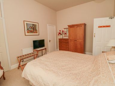 A bedroom with a double bed a wooden wardrobe a chest of drawers a television on a small table and a wooden luggage rack at Sandsend Sunset View in Whitby
