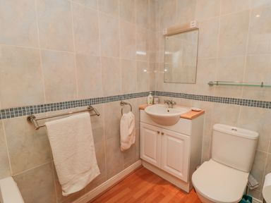A bathroom with a toilet sink cabinet mirror towel rails and tiled walls at Sandsend Sunset View Whitby