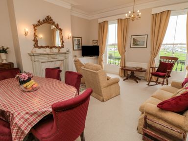 A living room with red chairs around a table and beige sofas by windows at Sandsend Sunset View in Whitby