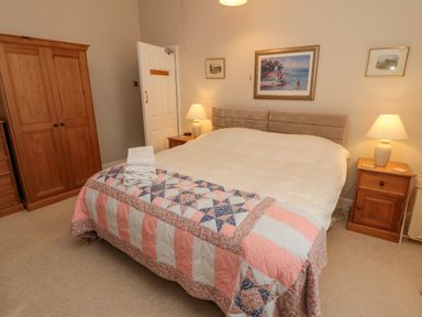 A bedroom with a double bed covered with a quilt and towels on top a wooden wardrobe bedside tables with lamps and paintings on the wall at Sandsend Sunset View in Whitby