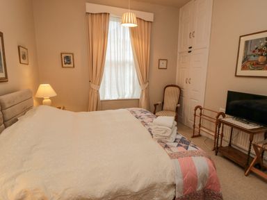 A bedroom with a bed linens and rolled towels a chair a table with a television and curtains at Sandsend Sunset View in Whitby