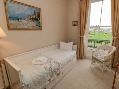 A bedroom with a single bed a wicker chair and a window showing grass and buildings at Sandsend Sunset View in Whitby