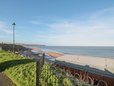 A coastal view with a sandy beach ocean and buildings on a grassy cliff at Sandsend Sunset View in Whitby