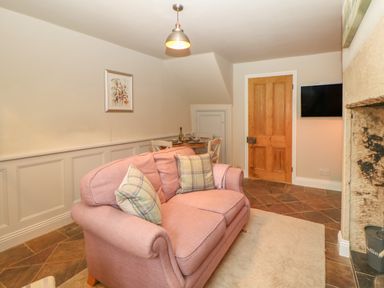 A sitting room with a pink sofa cushions a dining table wooden door and a wall-mounted television at Chapel Cottage in Corbridge