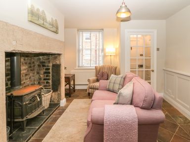 A living room with a fireplace a pink sofa and a striped armchair at Chapel Cottage in Corbridge