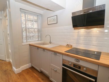 A kitchen with a wooden countertop sink electric stove oven and a window with blinds at Chapel Cottage in Corbridge
