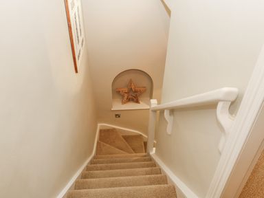 A carpeted stairway with a white handrail and a decorative wooden star in a wall niche at Chapel Cottage in Corbridge