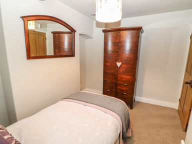 A bedroom with a bed a wooden wardrobe a mirror on the wall and a wooden door at Chapel Cottage in Corbridge