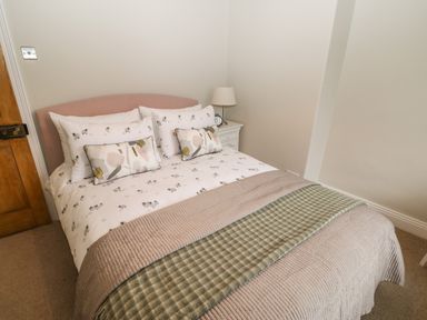 A bedroom with a double bed with patterned bedding and a bedside table with a lamp and clock at Chapel Cottage in Corbridge