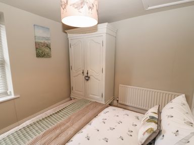 A bedroom with a bed and a white wardrobe next to a radiator and a window with blinds at Chapel Cottage in Corbridge