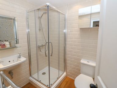 A bathroom with a corner shower cubicle a white toilet a small sink and a mirrored cabinet on the wall at Chapel Cottage in Corbridge