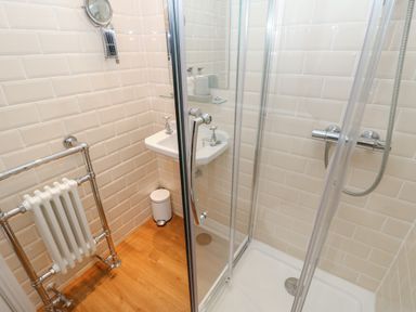 A bathroom with a shower enclosure a small sink a towel radiator and a waste bin at Chapel Cottage in Corbridge