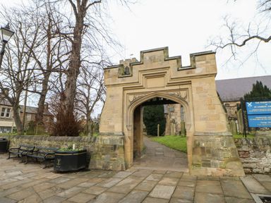 A stone archway entrance with benches and flower planters in a paved area at Chapel Cottage in Corbridge