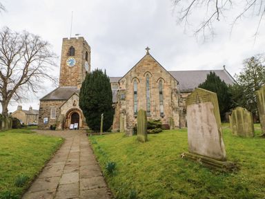 A stone church with a clock tower surrounded by gravestones and green grass