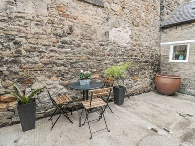 An outdoor patio with a round table and three chairs against a stone wall at Chapel Cottage in Corbridge