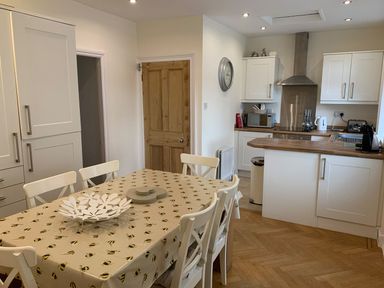A kitchen with white cabinets a wooden countertop a dining table with chairs and a bee patterned tablecloth at A Stone's Throw in Alnmouth