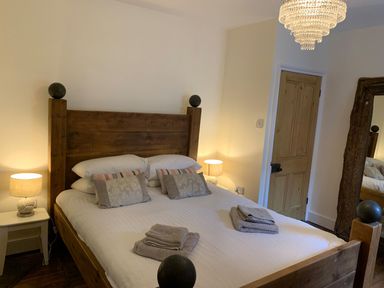 A bedroom with a wooden bed frame white bedding two bedside tables with lamps a wooden door and a large rustic mirror at A Stone's Throw in Alnmouth