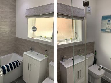 A bathroom with a bathtub a white sink cabinet a toilet and a window with small potted plants at A Stone's Throw in Alnmouth