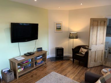 A living room with a wall mounted television wooden shelves and a leather chair at A Stone's Throw in Alnmouth