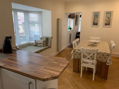 A dining area with a table covered by a bee patterned tablecloth and four chairs near a kitchen counter and window seat at A Stone's Throw in Alnmouth
