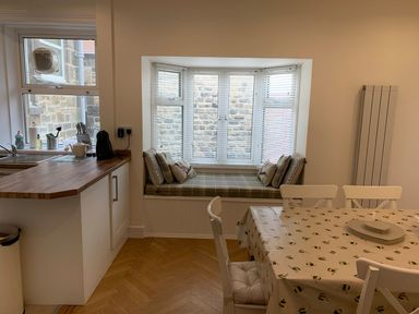 A kitchen with a wooden countertop, a window seat with cushions, and a dining table with bee patterned tablecloth at A Stone's Throw in Alnmouth