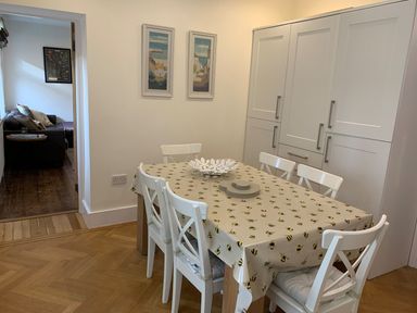 A dining area with a table covered by a bee-patterned tablecloth and six white chairs at A Stone's Throw in Alnmouth