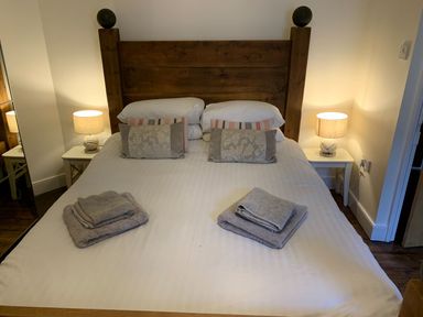 A bedroom with a wooden bed frame two bedside tables with lamps and folded towels on the bed at A Stone's Throw in Alnmouth