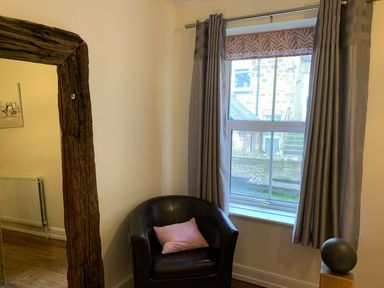 A corner of a room with a black leather armchair and pink pillow near a window with curtains at A Stone's Throw in Alnmouth